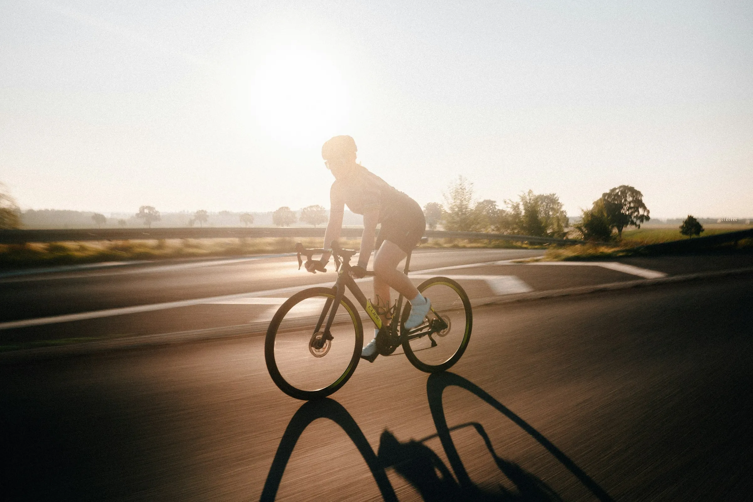 A cyclist riding an open road in daylight — steady effort, not a sprint.